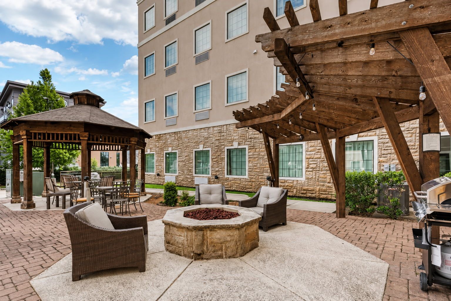 image Unwind around the stone fire pit under the wooden pergola strung with string lights.