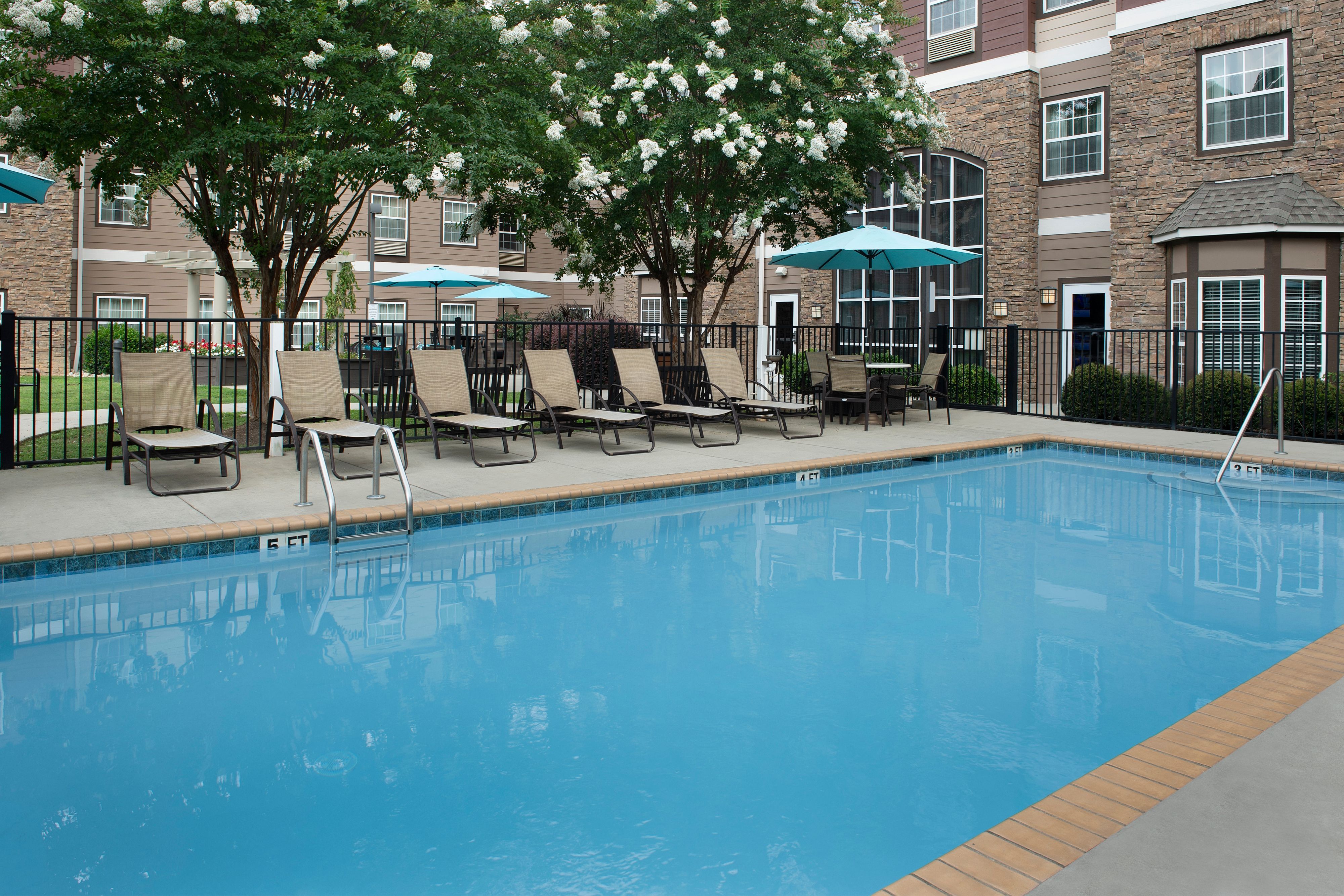 image Tranquil outdoor pool area with lush trees and relaxing loungers.