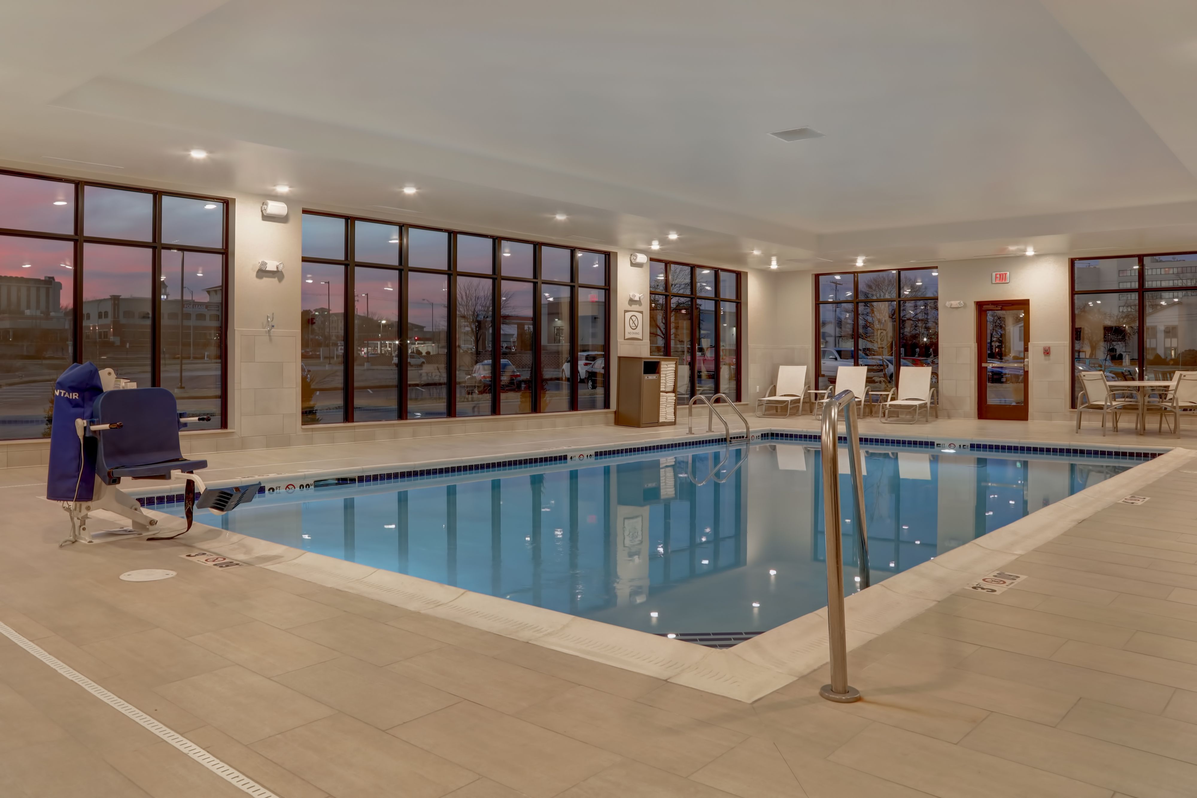 image Heated indoor pool surrounded by large windows and lounge chairs.