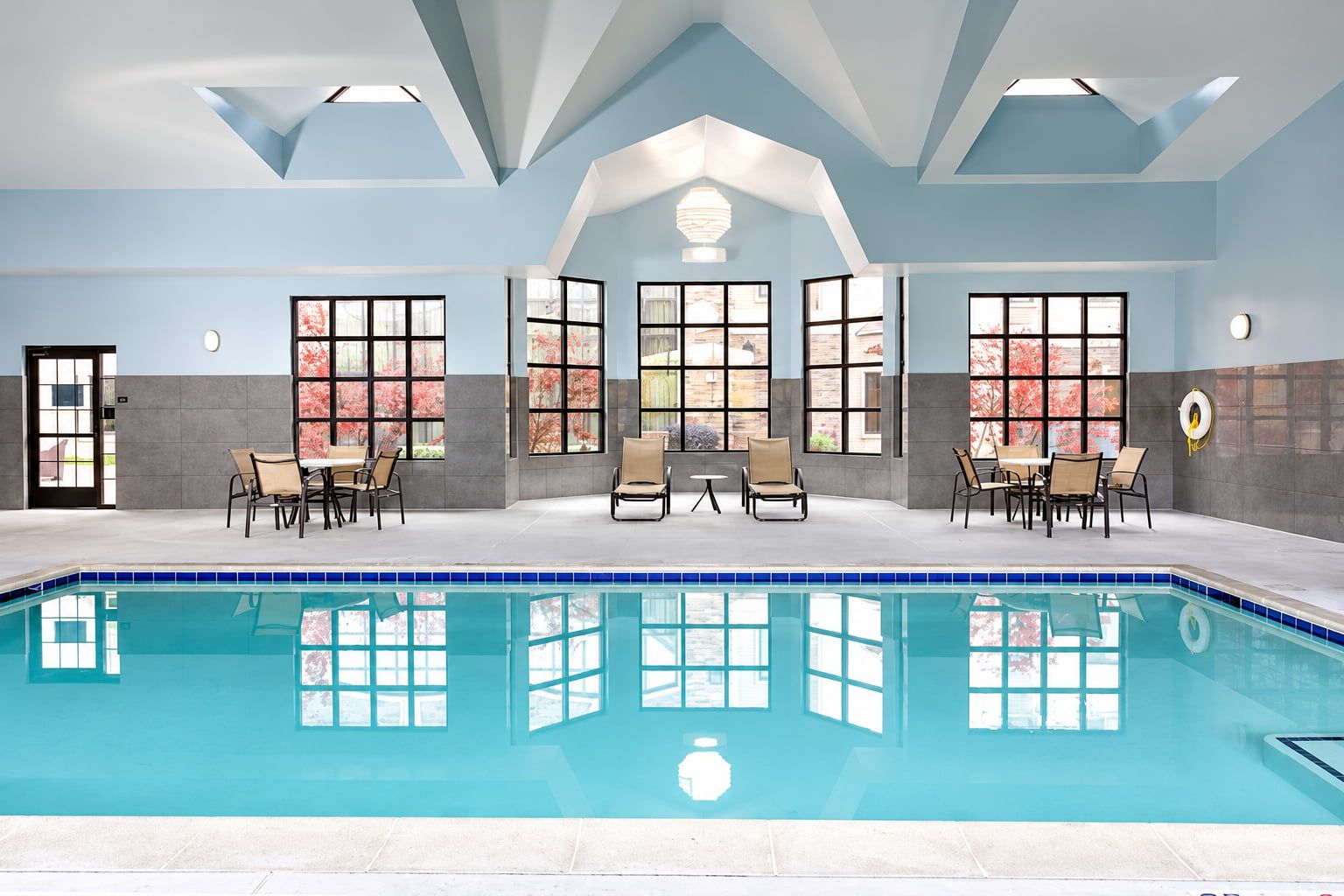 image Indoor swimming pool with a tiled pool deck, large windows, and lounge seating.