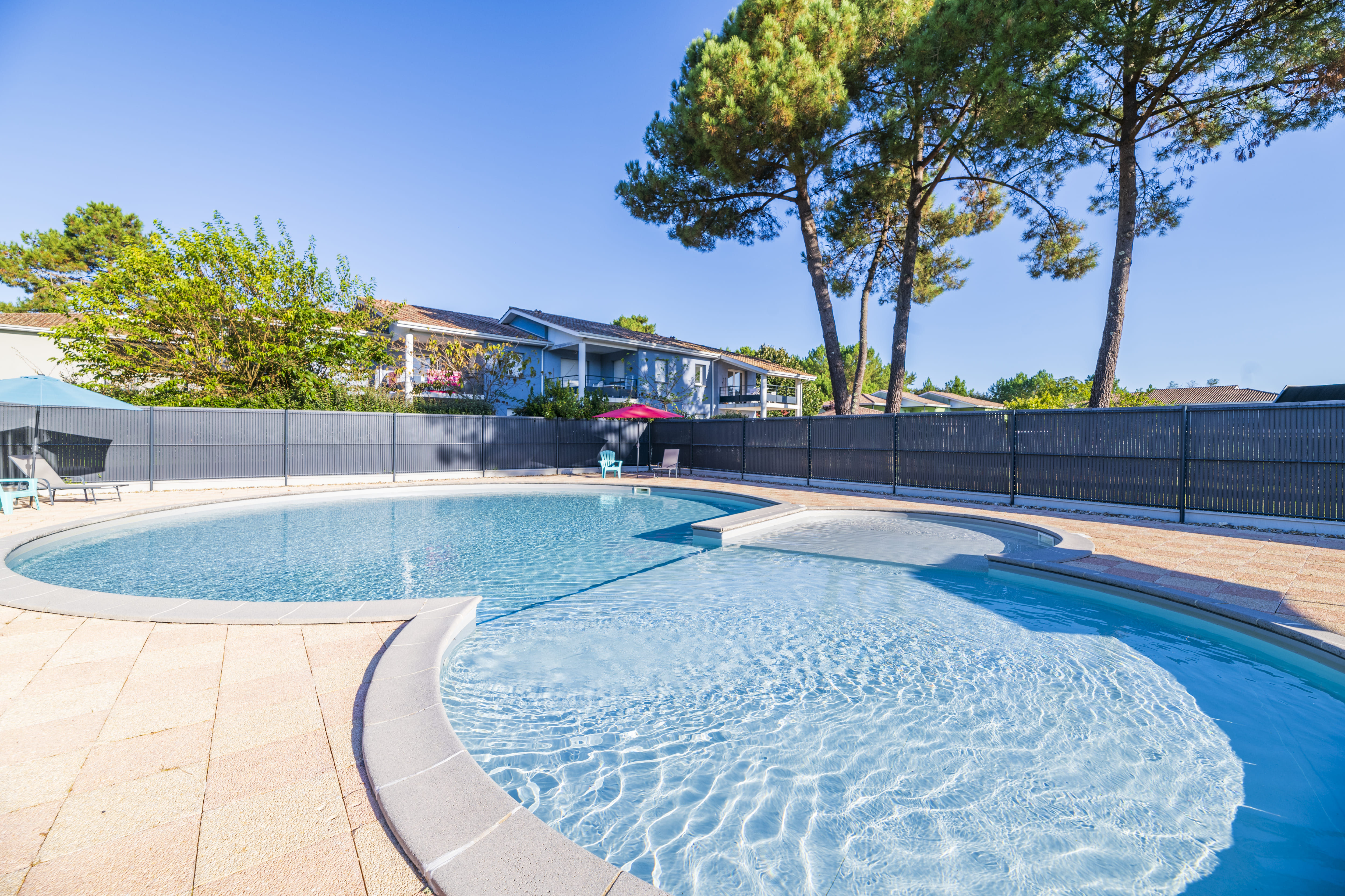image Ease into the curved outdoor pool, framed by pine trees and a sunny terrace.