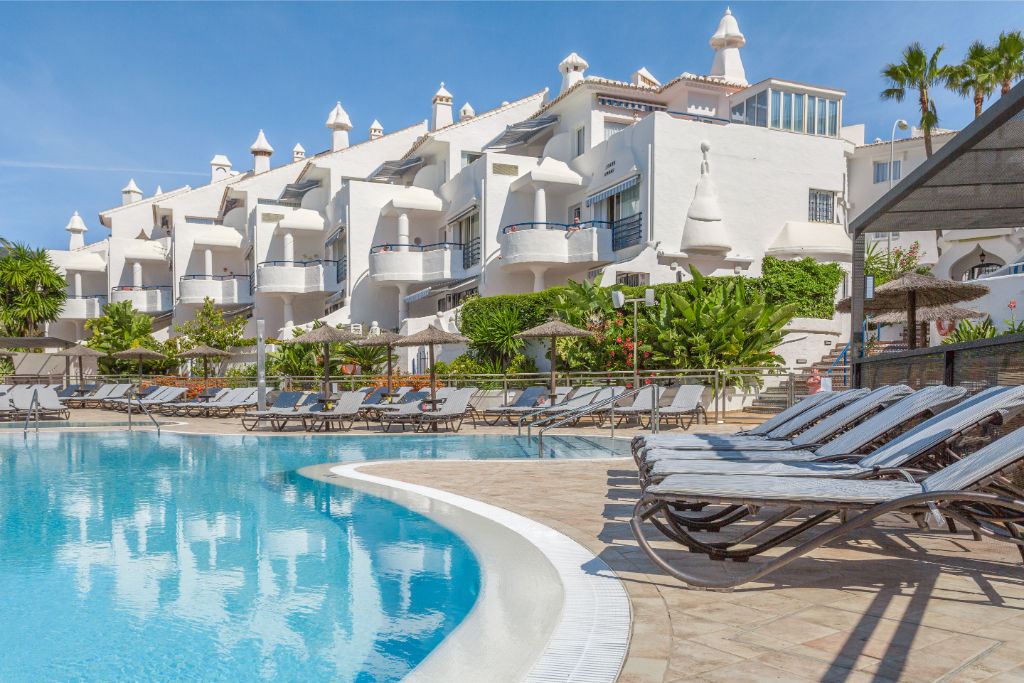 image Curved pool surrounded by palm trees and white villas, an idyllic setting for leisure and relaxation.