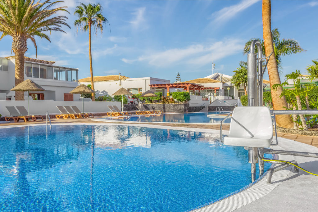 image Sunlit pool deck with inviting crystal-clear waters, framed by a stunning vista.