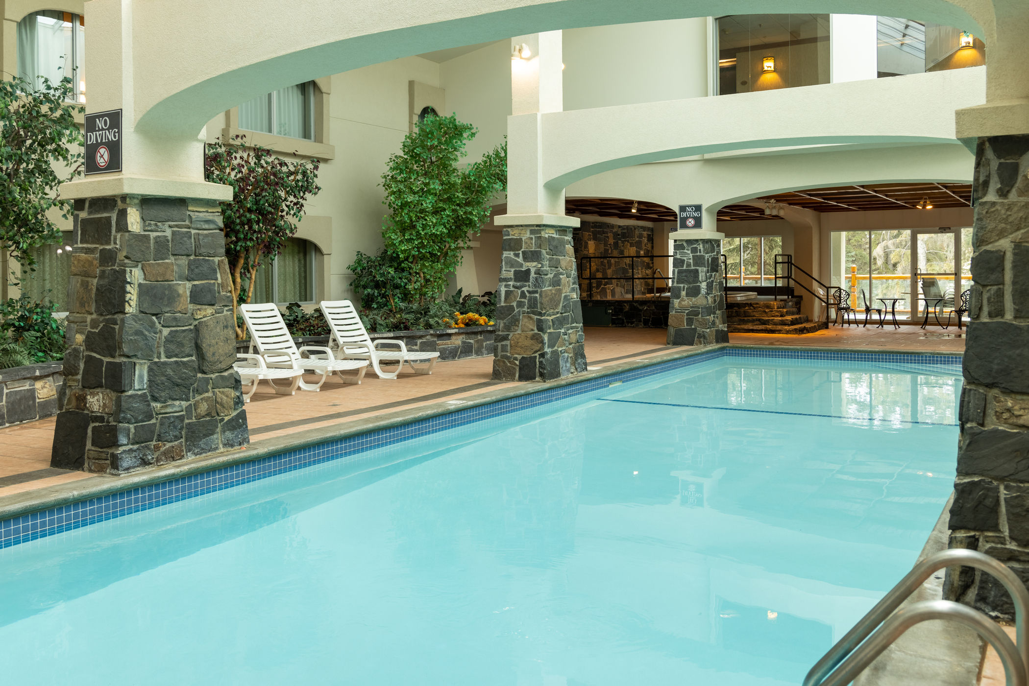 image Indoor pool lined with grey stone columns and white lounge chairs under a two-story atrium
