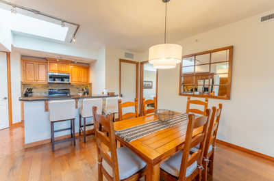 Dining area with wooden table, lamp, and kitchen in background