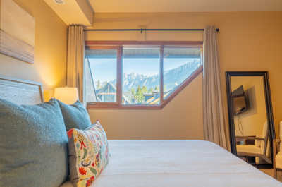 Bed with blue pillows and lamp, window showing mountains