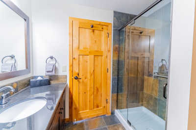 Bathroom with glass shower, wooden accents, and granite sink