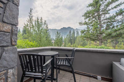 Balcony with two chairs, table, and trees in the background