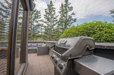 Grill on balcony next to seating area and shrubs