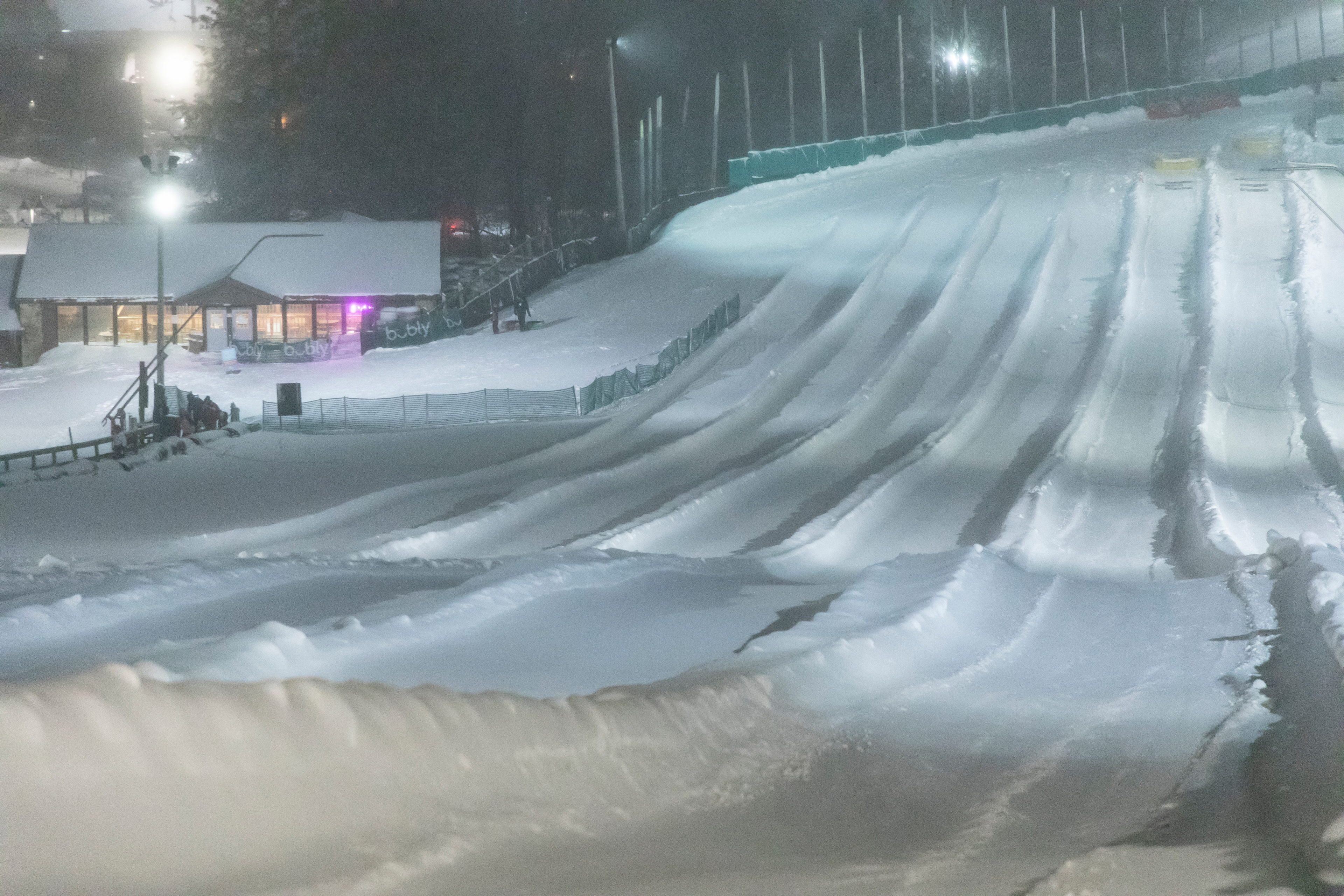 image Illuminated by soft lights, the snow-tubing lanes create a magical scene, carving through the winter landscape and beckoning thrill-seekers under the night sky.