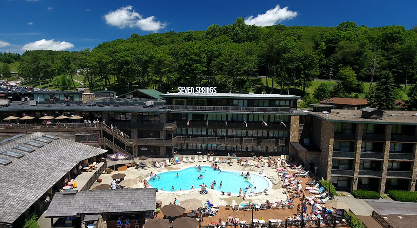 image The outdoor pool area bustles with life under a stunning azure sky, as guests bask in the warm sun with the majestic forest backdrop, perfect for summer fun.