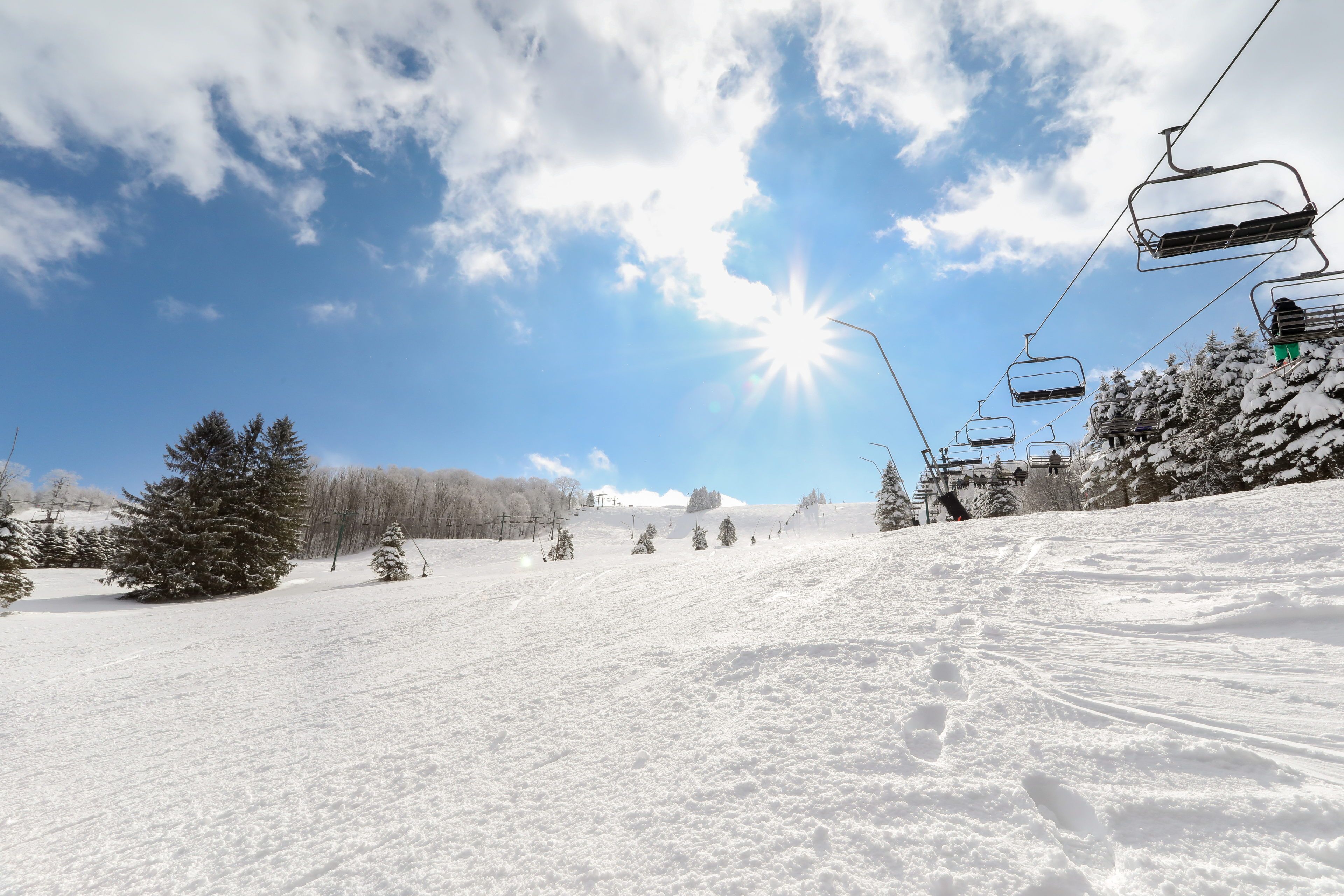 image Under a radiant sun with fluffy clouds drifting above, the pristine slopes and ski lifts beckon adventurers to explore the snowy trails and embrace the beauty of the outdoors.