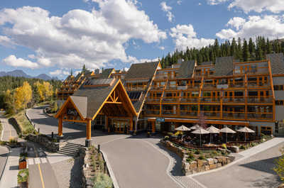 A stunning hotel entrance that welcomes you with its striking architecture and warm wooden design, set against the backdrop of lush trees and clear skies, inviting you to a memorable stay.