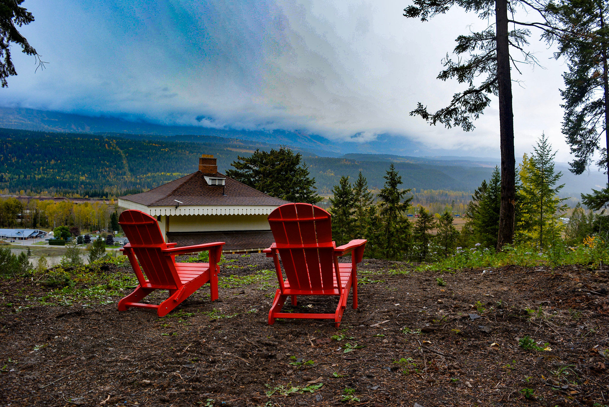 image Relax in vibrant red chairs, surrounded by towering trees and the allure of distant mountains.