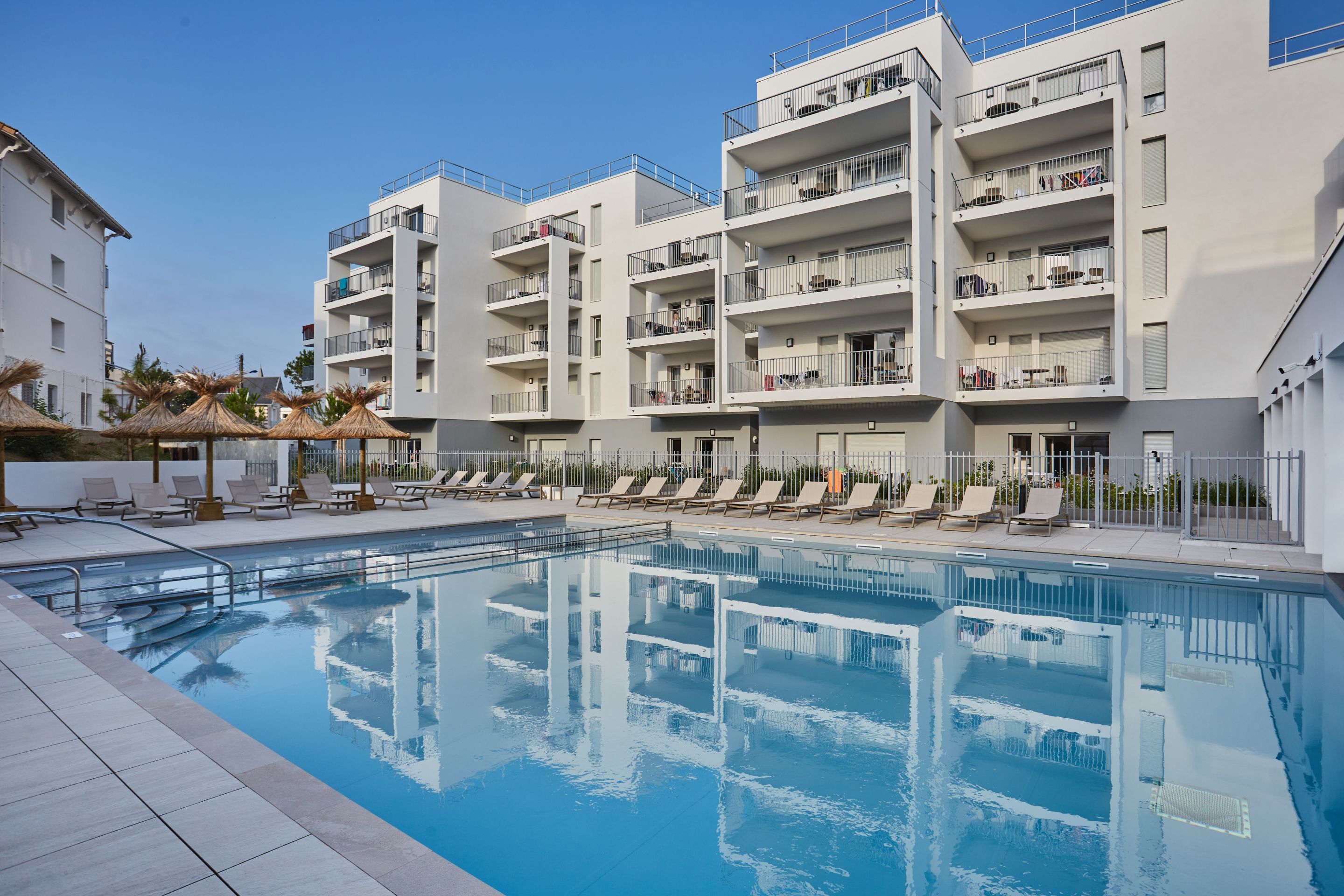 image Relax by the stunning outdoor pool, surrounded by modern apartment buildings and plenty of lounge chairs for sunbathing. Perfect for a refreshing dip or enjoying a sunny afternoon.