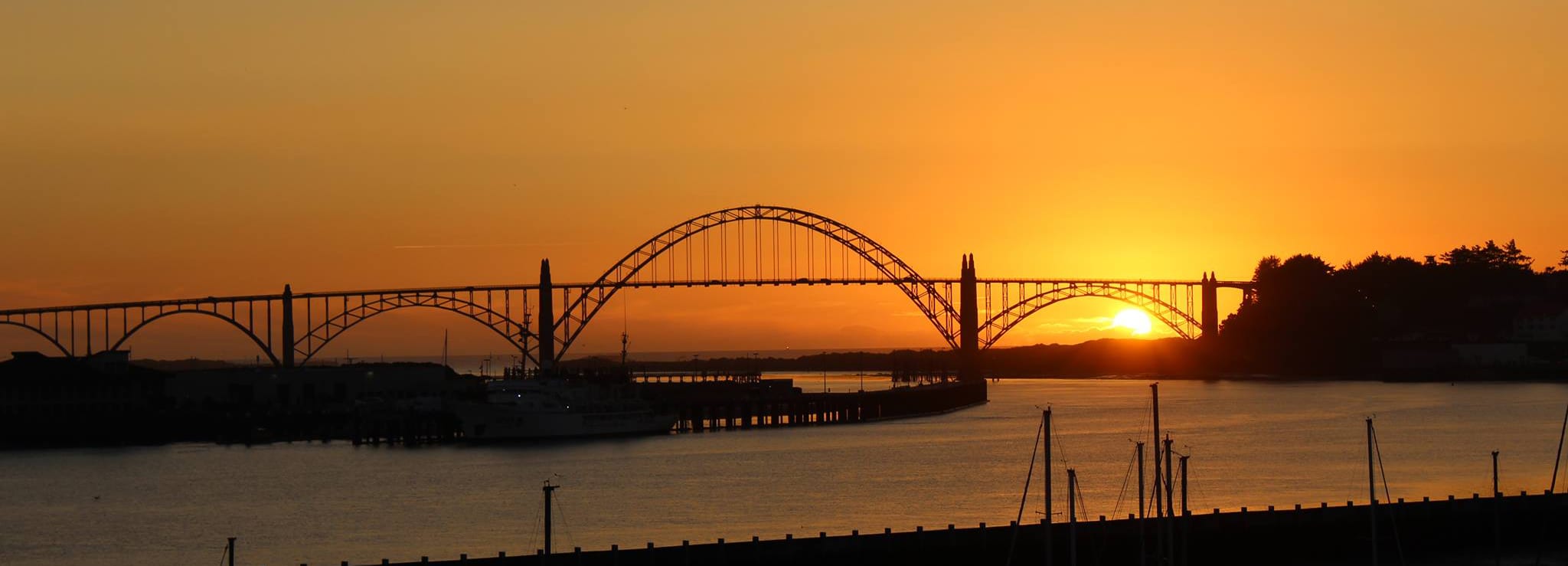image Watch the sun set over the water, casting a warm glow across the horizon and bridge.