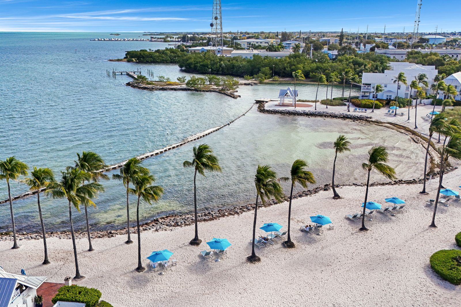 image Beachfront view with white sand, umbrellas, and a structure near the lagoon.