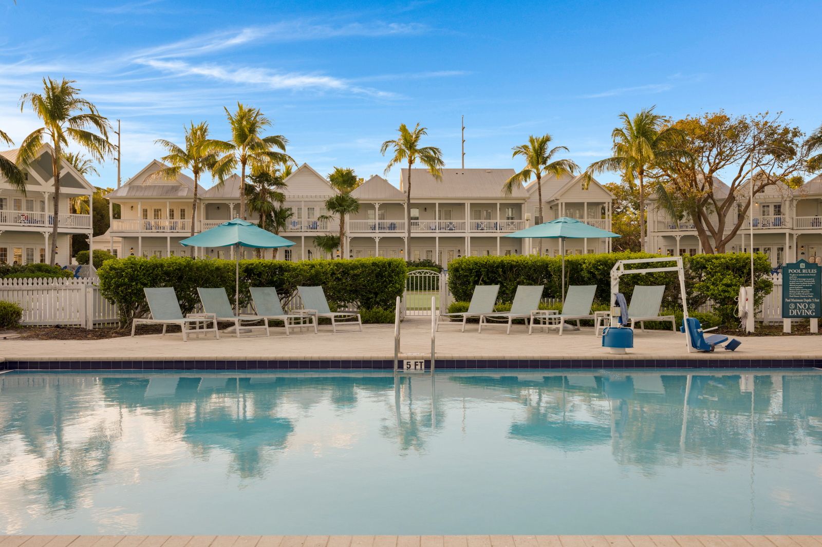 image Pool area with lounge chairs and palm trees reflected in the water.