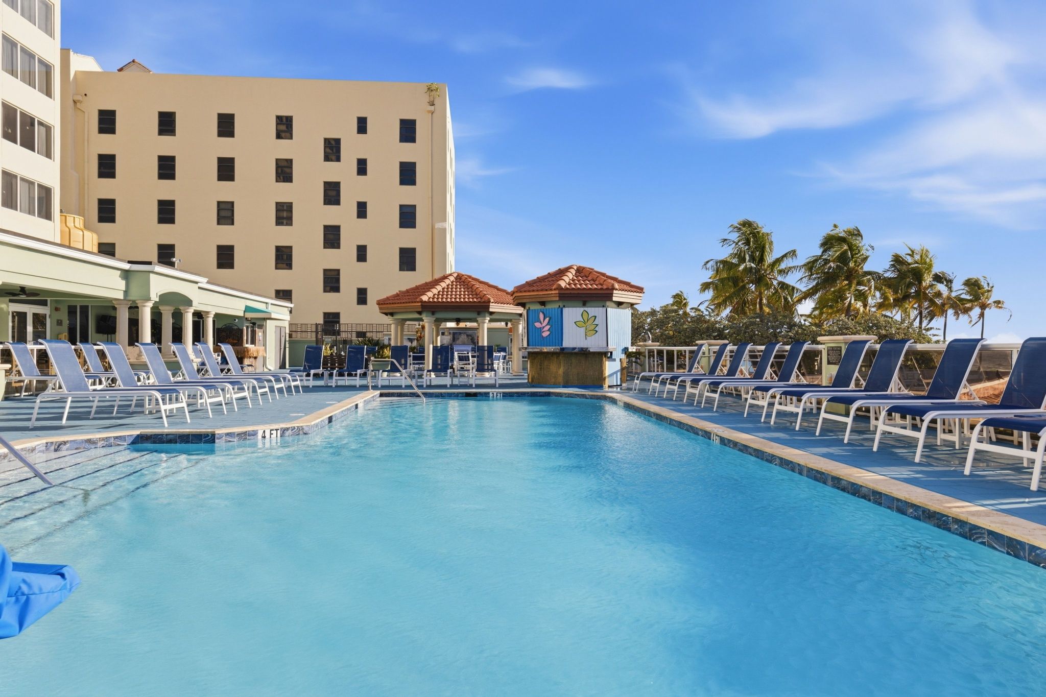 image Swimming pool with blue water, lounge chairs, and palm trees