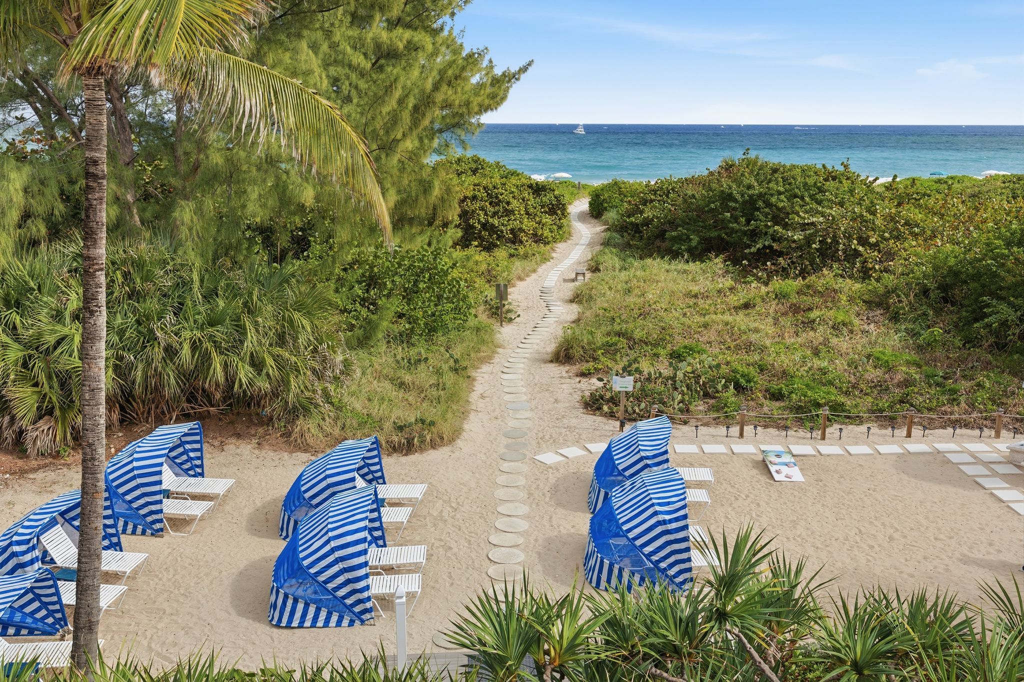 image Lounge chairs with striped canopies are arranged on the sandy beachfront, offering a relaxing spot steps from the ocean at Sand Dune Shores.