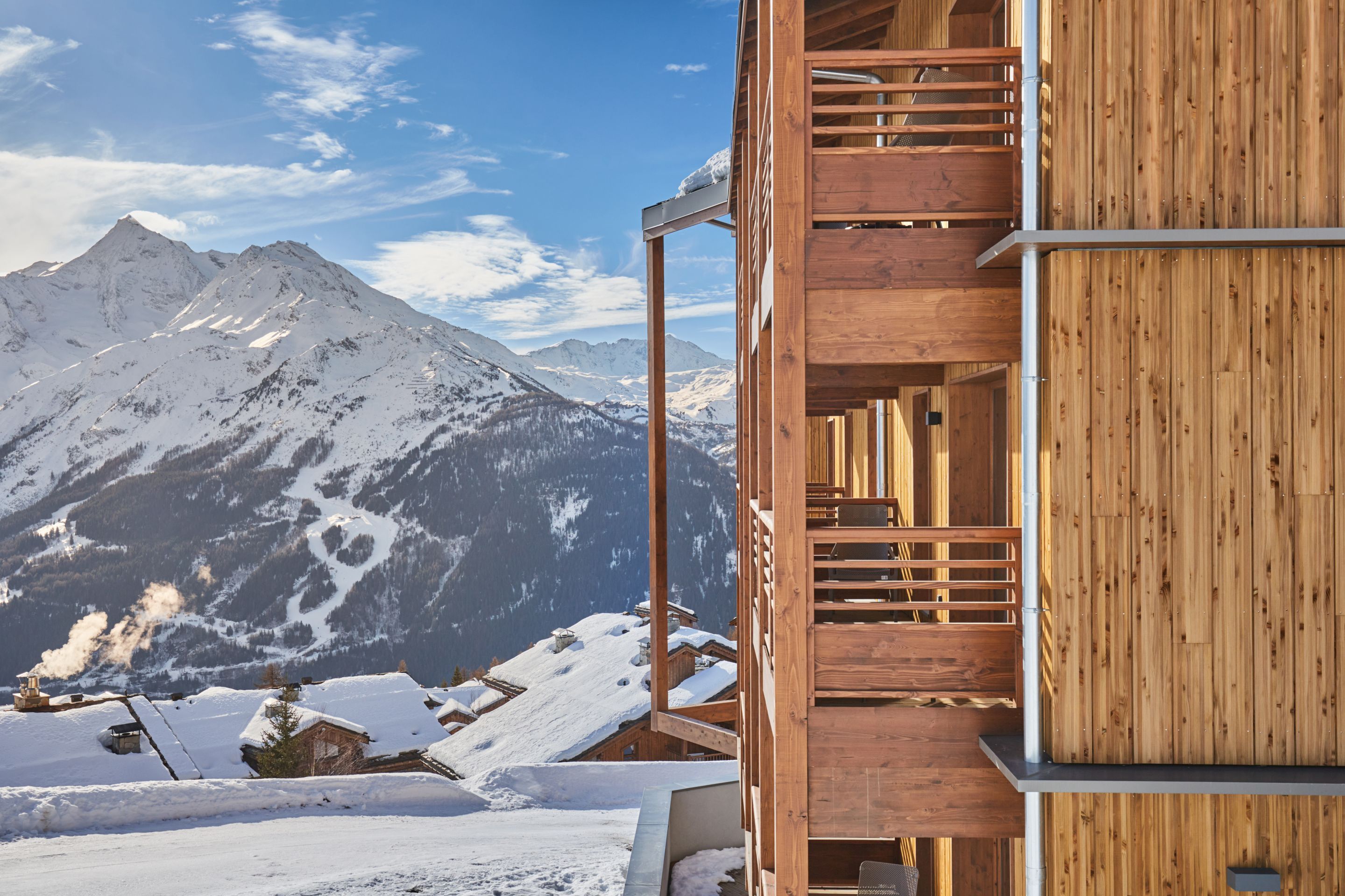 image Timber balconies and wooden facade of the residence, with alpine snow and mountain views stretching out behind.