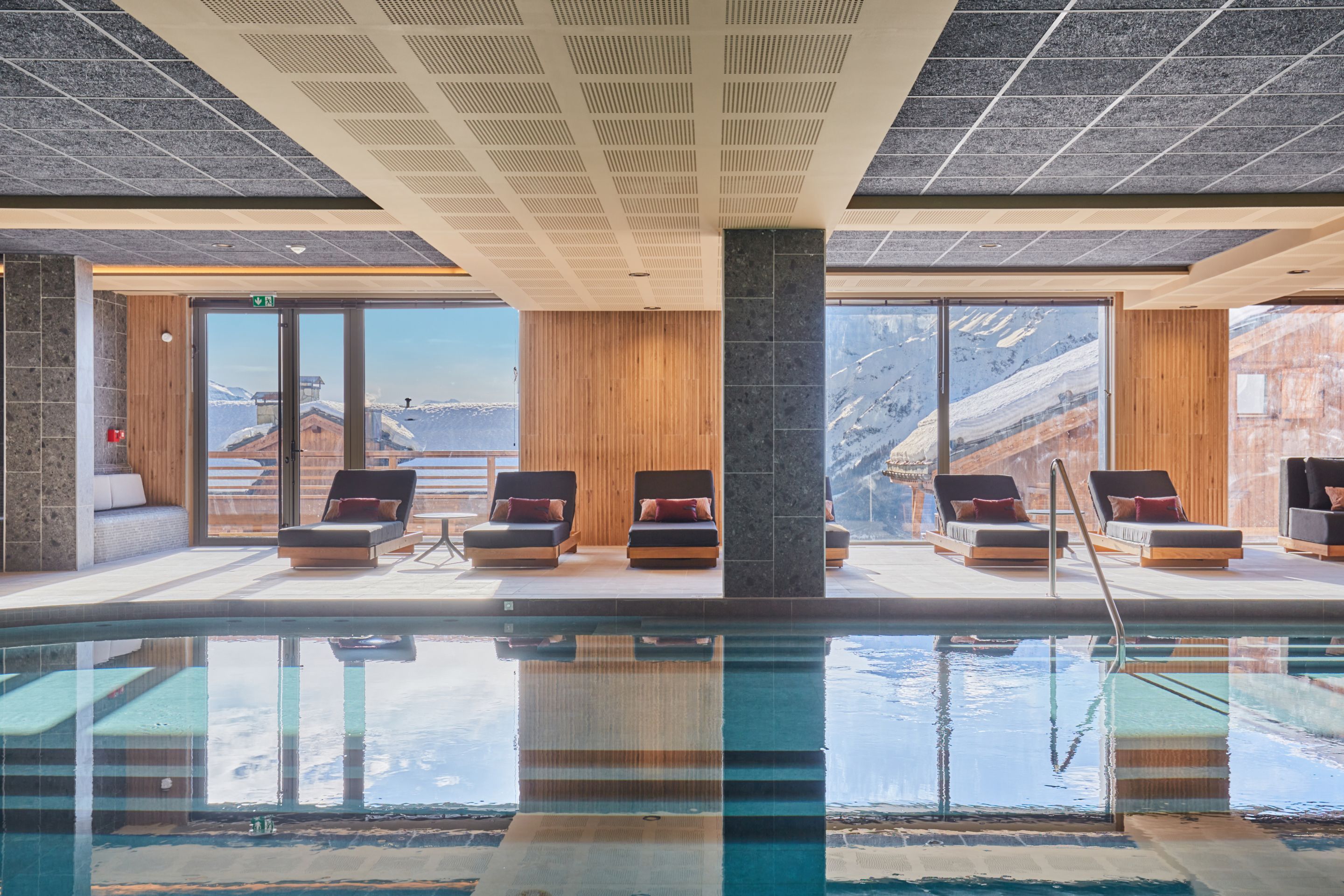 image Pool deck with dark loungers and mountain rooftops beyond the glass — natural light fills the space throughout the day.