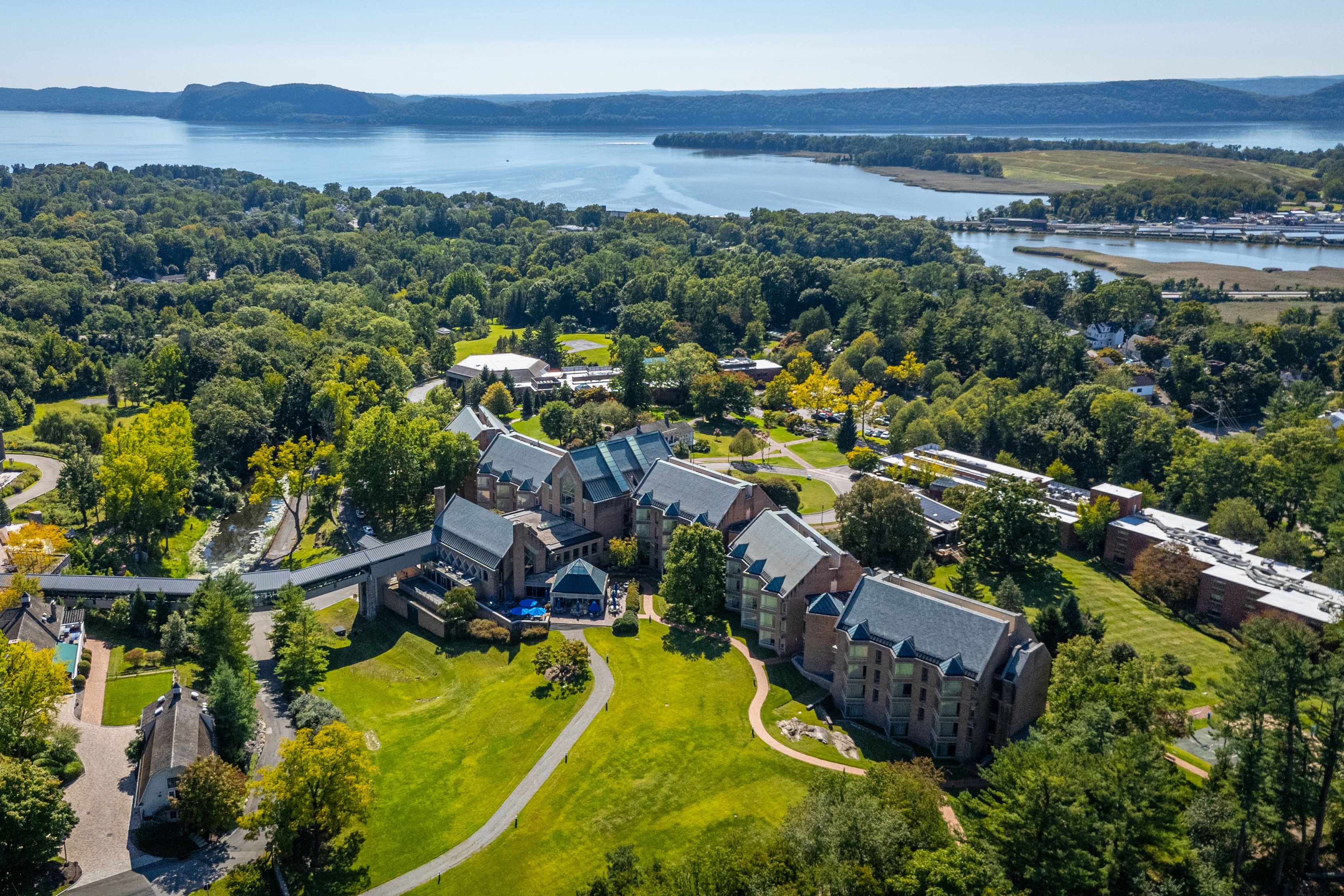 image A panoramic aerial view reveals the expansive grounds of Windrose on Hudson, nestled among lush greenery with the serene Hudson River creating a breathtaking backdrop.