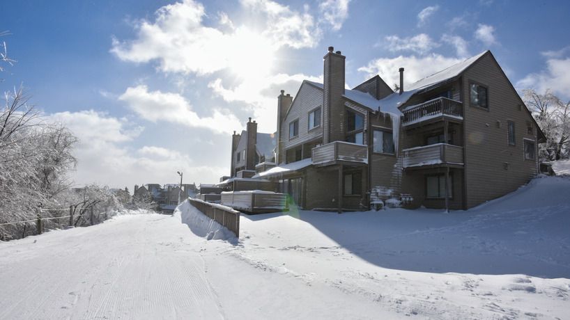 image Nestled amidst a serene blanket of snow, the charming Villages Condos at Seven Springs Resort gleam under a bright winter sun, inviting guests to enjoy a cozy retreat in Champion, Pennsylvania.