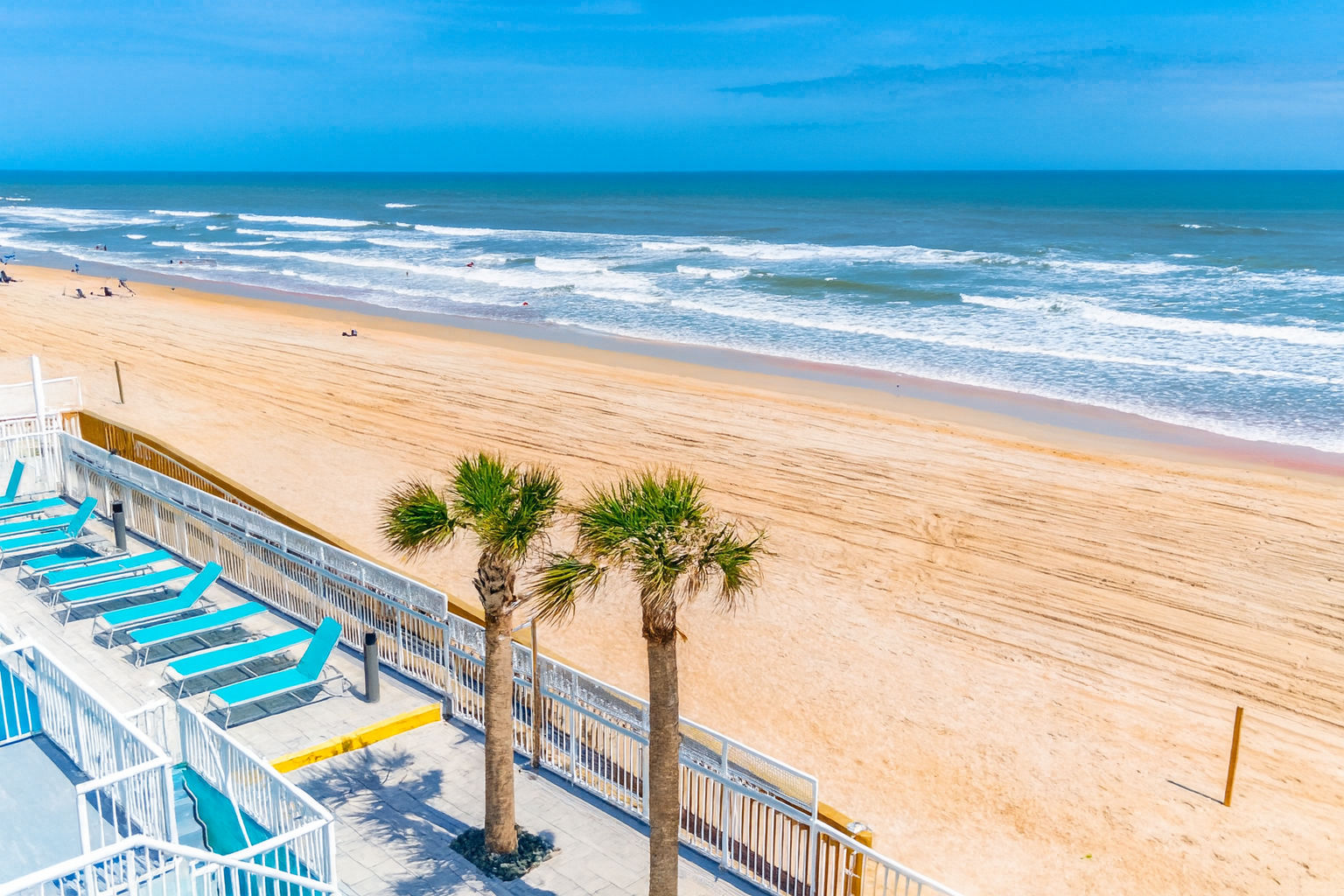 image Relax on the beachfront with lounge chairs and palm trees, just steps from the pristine sandy shores of Ormond Beach.