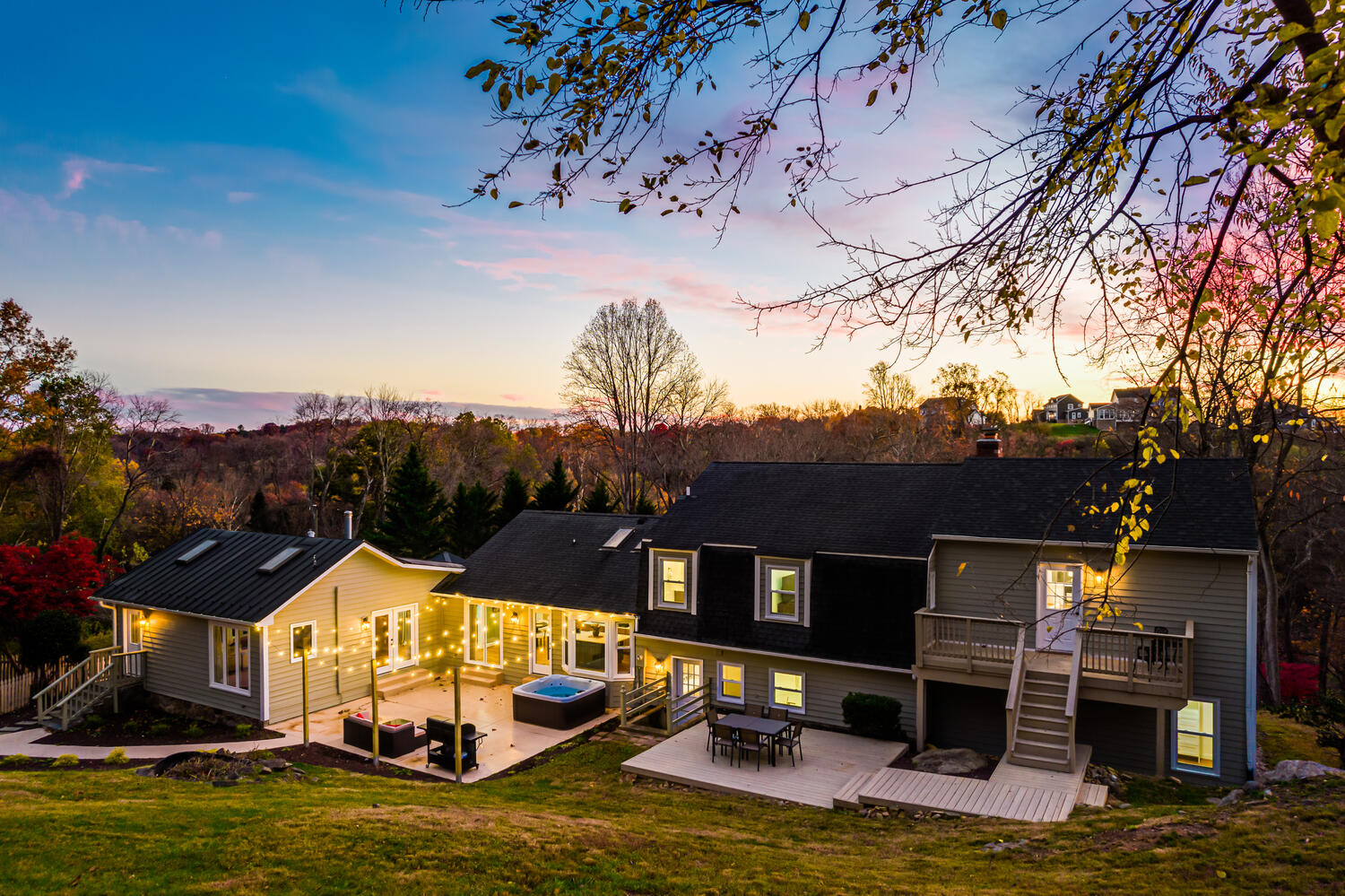 image Expansive outdoor area with hot tub and seating, surrounded by lush greenery beneath a glowing sunset sky.