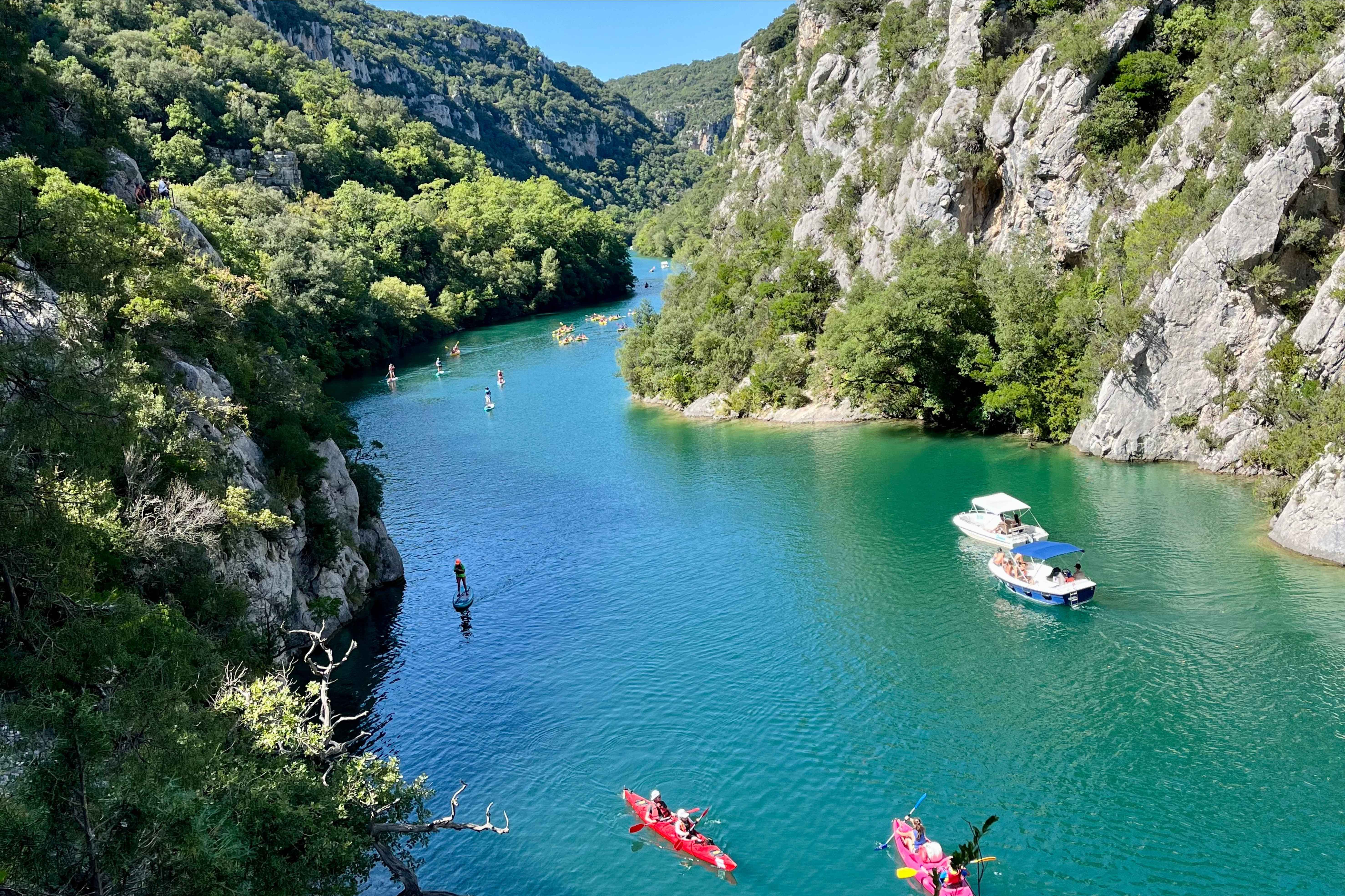 image Paddleboarders and kayakers enjoy the crystal-clear waters of the Verdon River, surrounded by lush greenery and towering cliffs.