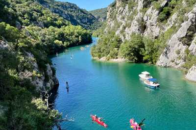 Paddleboarders and kayakers enjoy the crystal-clear waters of the Verdon River, surrounded by lush greenery and towering cliffs.
