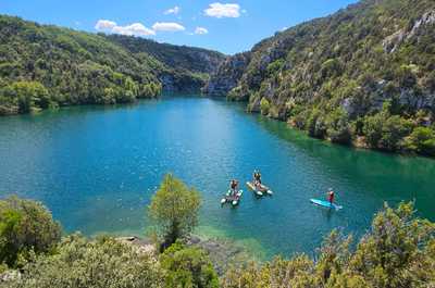 Paddleboarders glide across the serene turquoise waters, surrounded by lush green hills that emphasize the peaceful ambiance of Camping Verdon Les Grands Domaines.