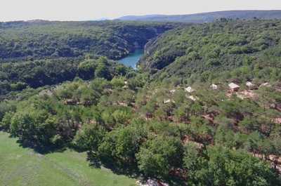 An aerial view showcases the verdant forest canopy enveloping Camping Verdon, with its proximity to the shimmering river nestled amongst the vivid greenery.