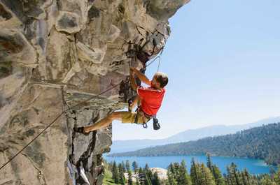 A climber scales a rocky cliff with determination, fueled by the stunning views of the forest and lake below.