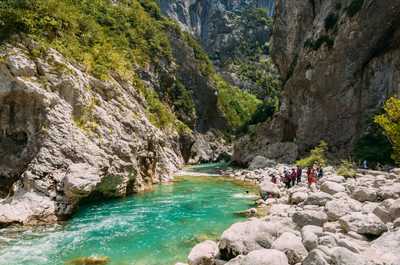 Families gather along the rocky shore, soaking in the beauty of the river's vibrant hues and the breathtaking canyon landscape.