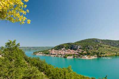 The vibrant blue water of the lake contrasts beautifully with the lush hills and quaint village, embodying the serene experience that Camping Verdon offers.