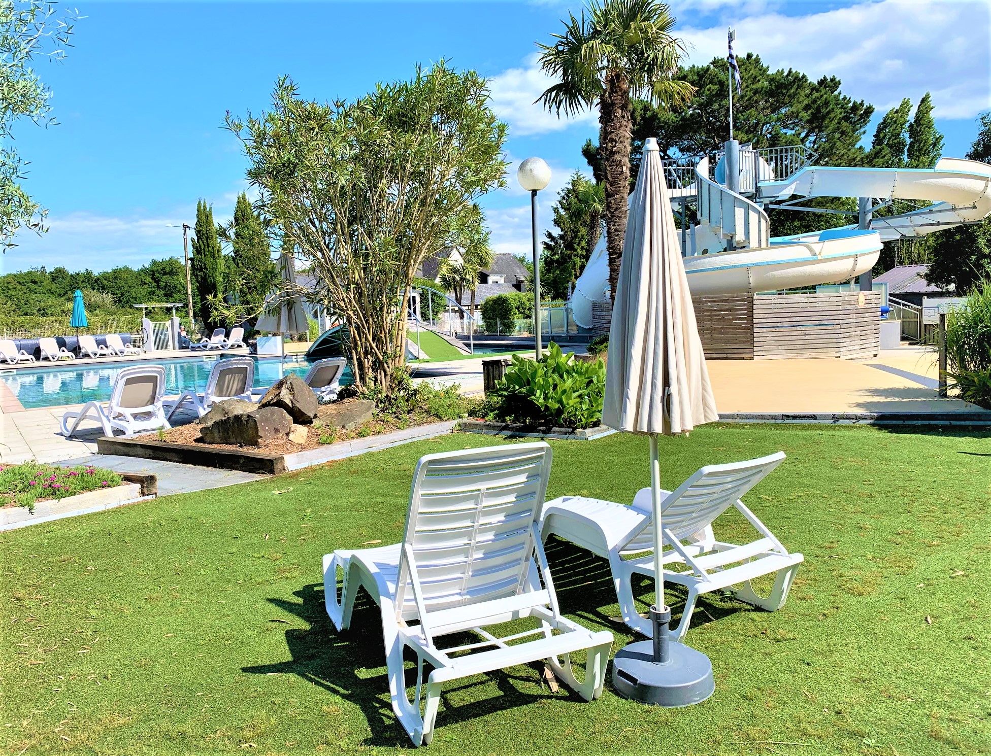 image Relaxation awaits on the sun loungers by the pool, nestled in green gardens with a view of the adventurous water slide.