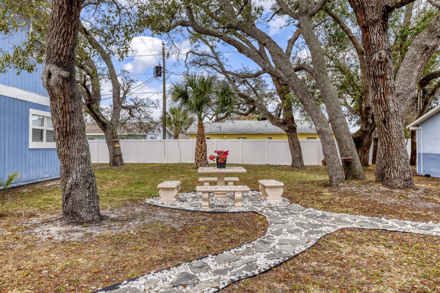 image Quiet patio space with a stone picnic table surrounded by mature trees and bordered by blue and yellow buildings.