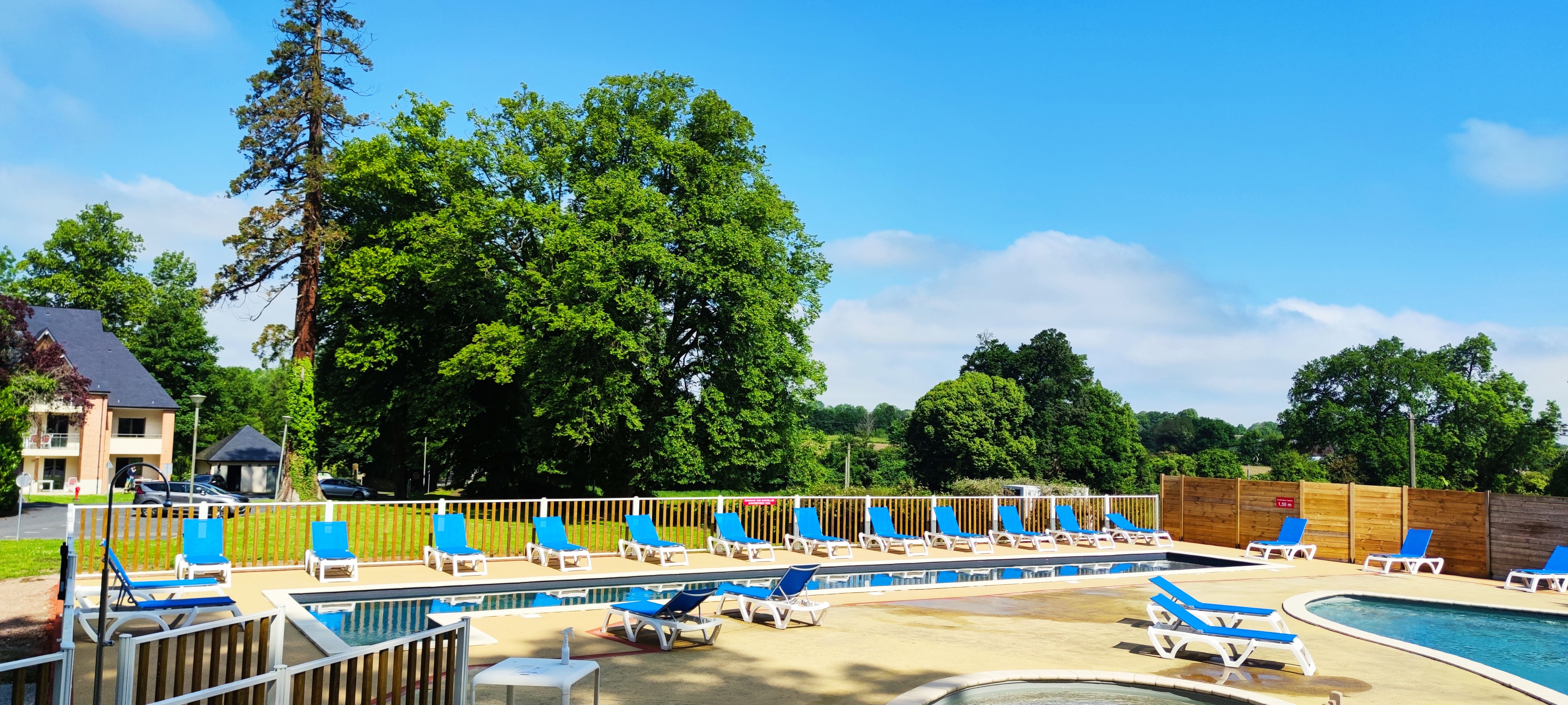 image Sun loungers line the poolside, backed by the tall trees of the surrounding park