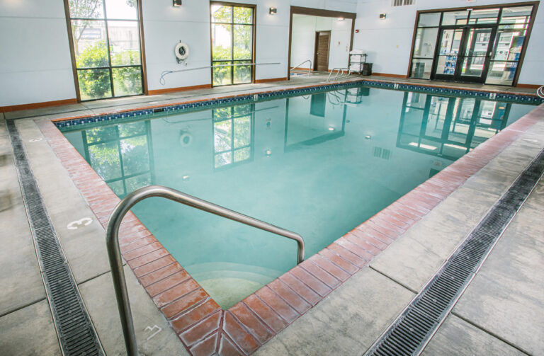 image Tiled indoor pool with steps into the water and large windows overlooking garden greenery.