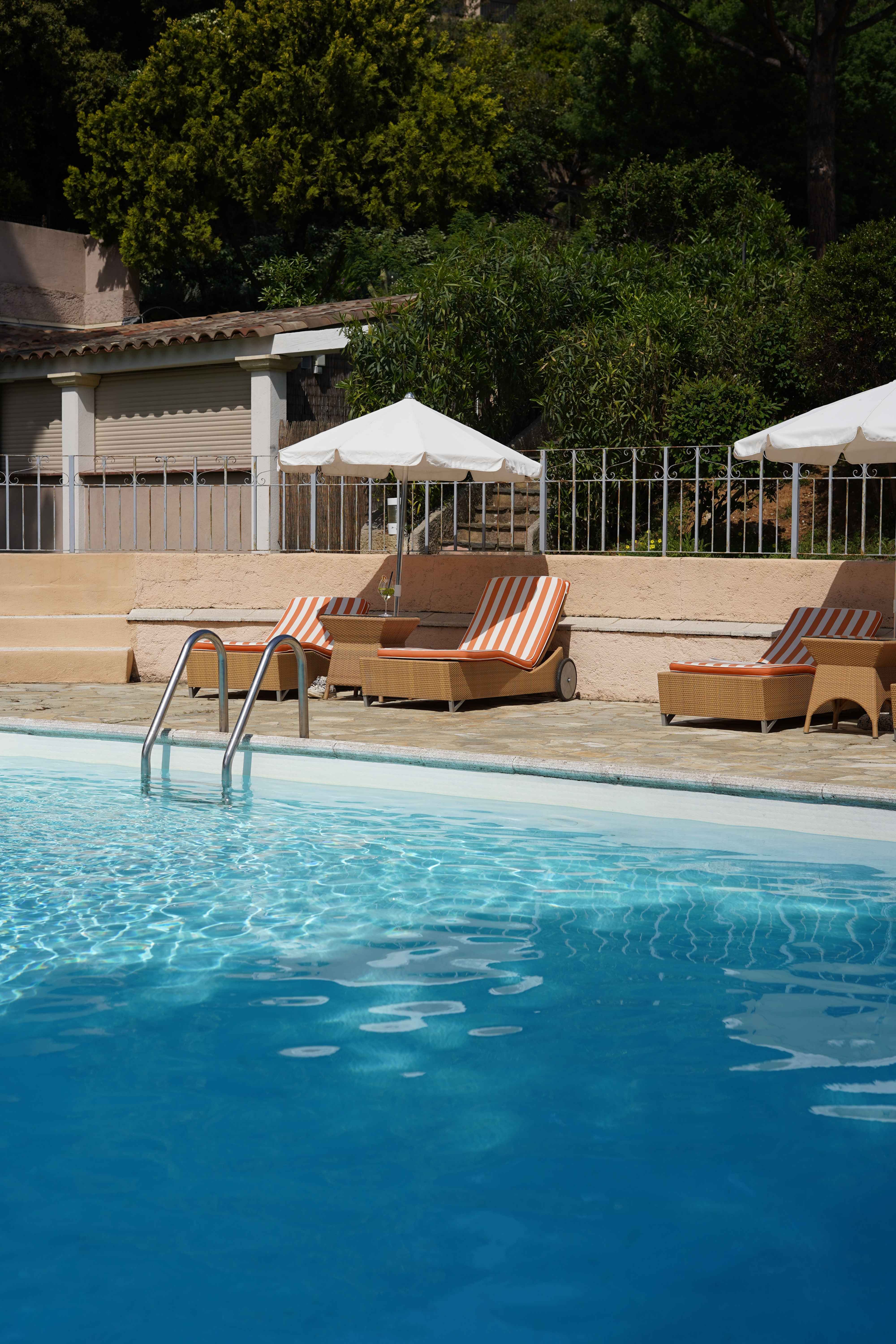 image Blue pool water with striped lounge chairs and clipped hedges — afternoons here move slowly