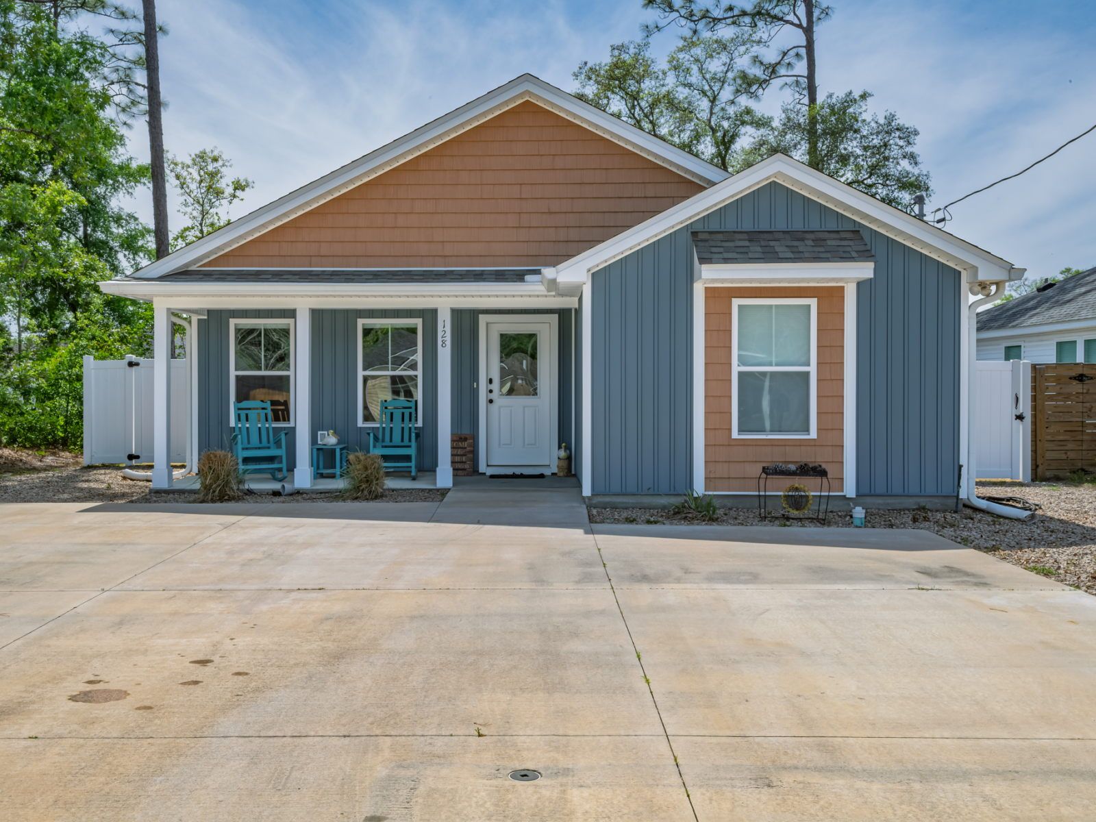 image Front exterior with blue-gray siding, brown upper section, teal chairs, white door, and concrete driveway
