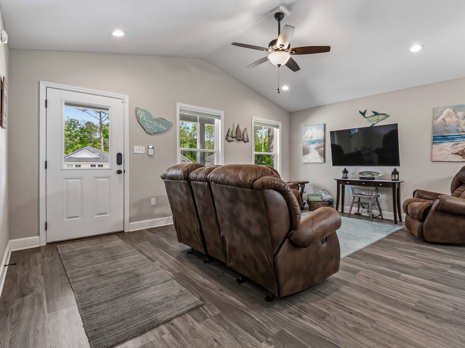 image Living room with brown recliner, ceiling fan, wall-mounted TV, and front door