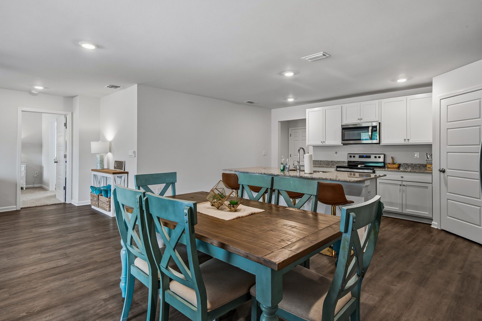 image Dark wood dining table with six turquoise chairs, open to the kitchen with white cabinets and stainless appliances