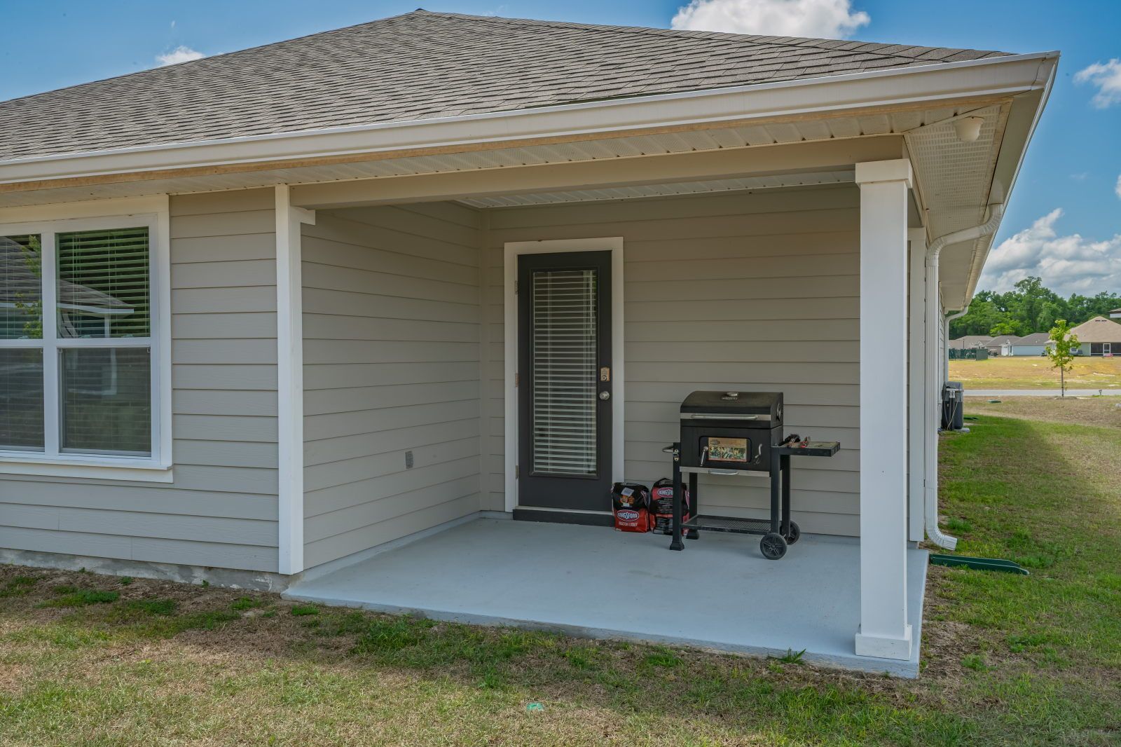 image Covered back porch with a black charcoal grill on a cart and two bags of charcoal beside a glass-panel door