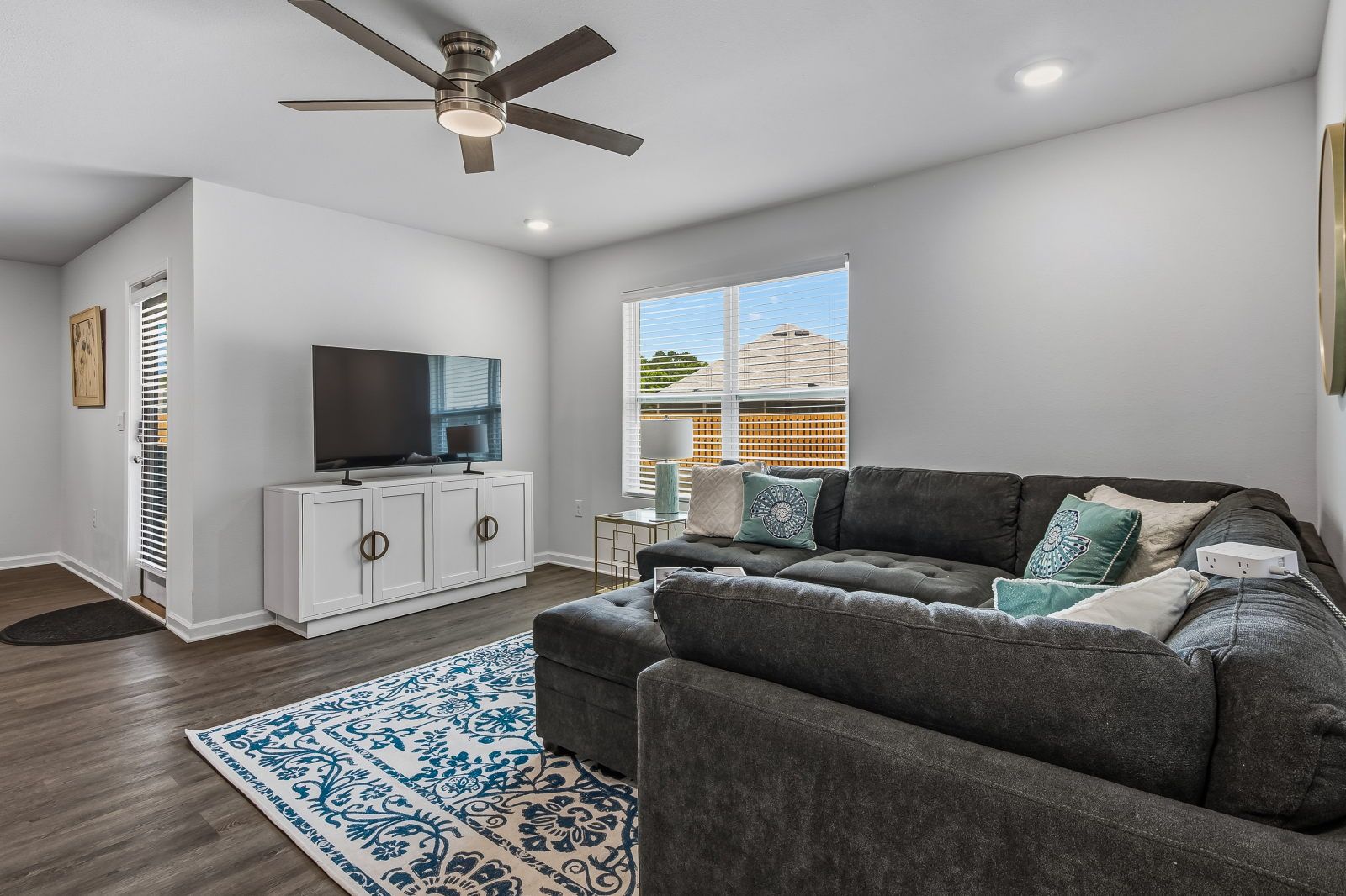 image Dark gray sectional sofa on wood-look floors, white media cabinet with flat-screen TV, and a blue-patterned area rug