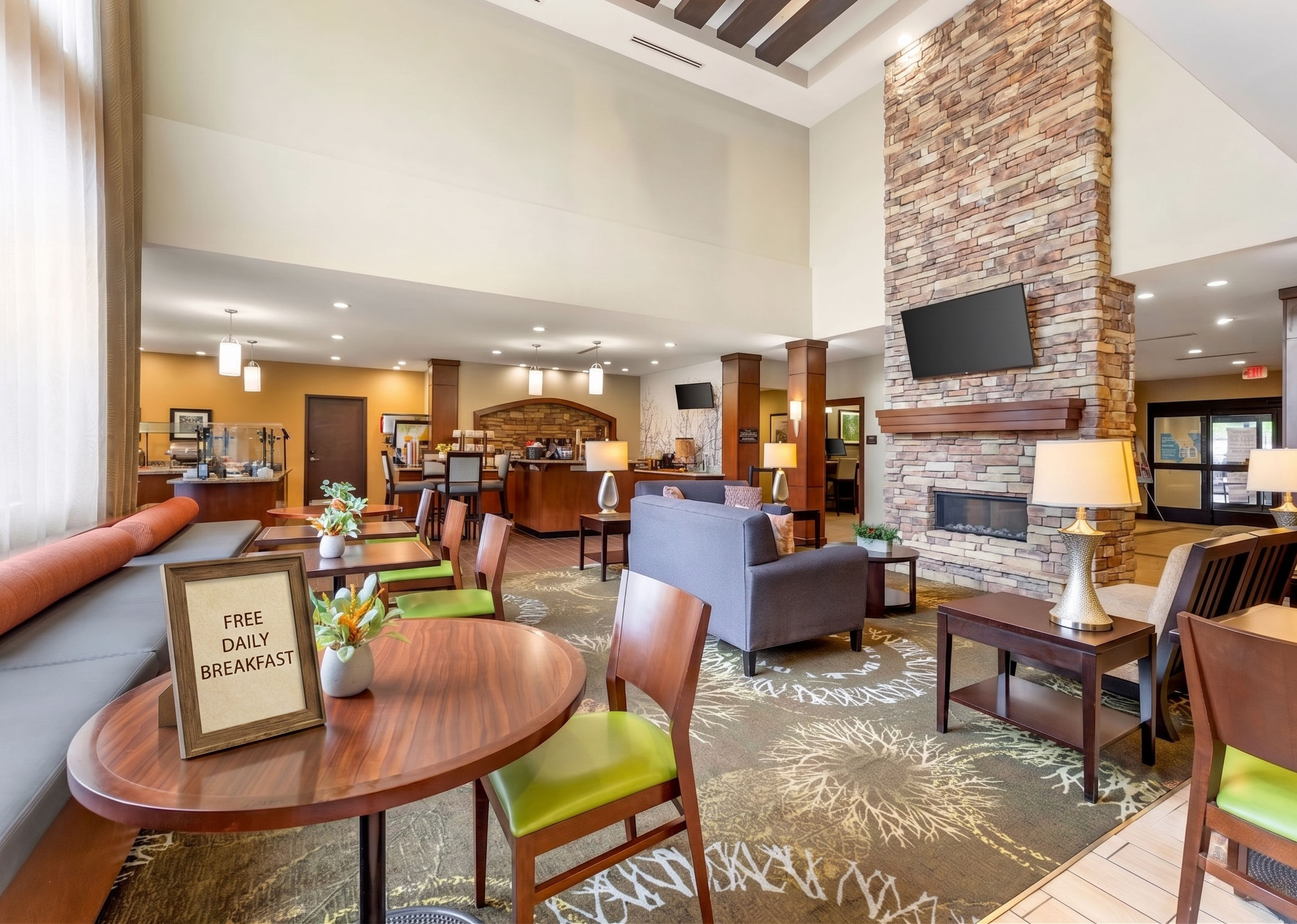 image Enjoy FREE DAILY BREAKFAST. Comfortable lounge area with seating, plants, and fireplace.