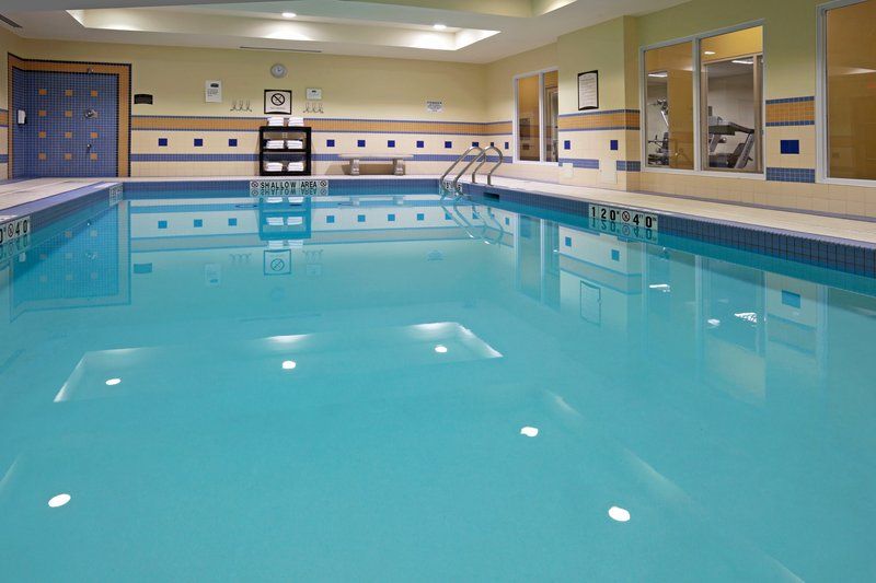 image Indoor pool with clear blue water, accessible stairs, and fitness area visible behind glass.