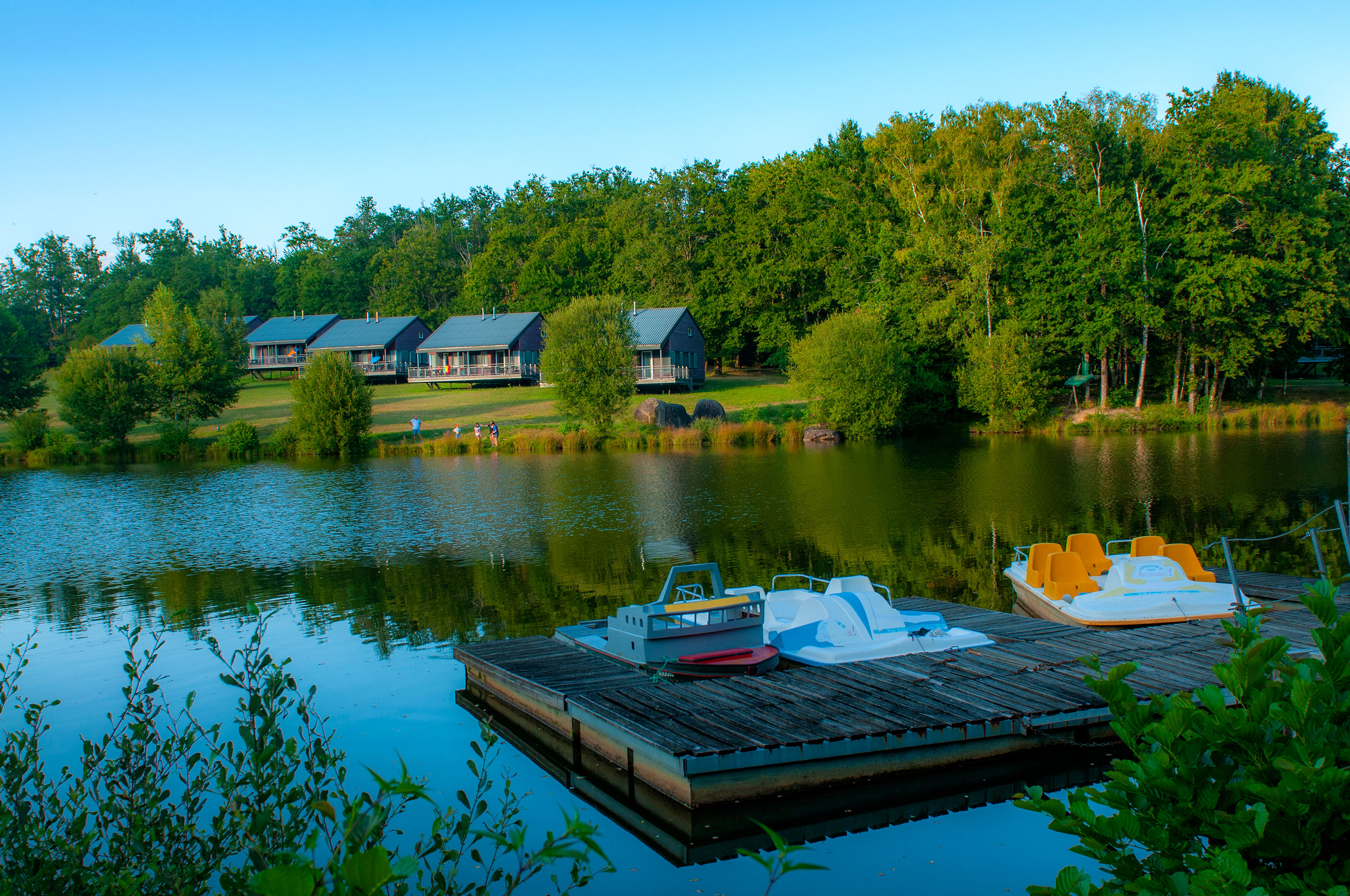 image Pedal boats at the wooden dock, with three chalets nestled among the trees alongside the lake.